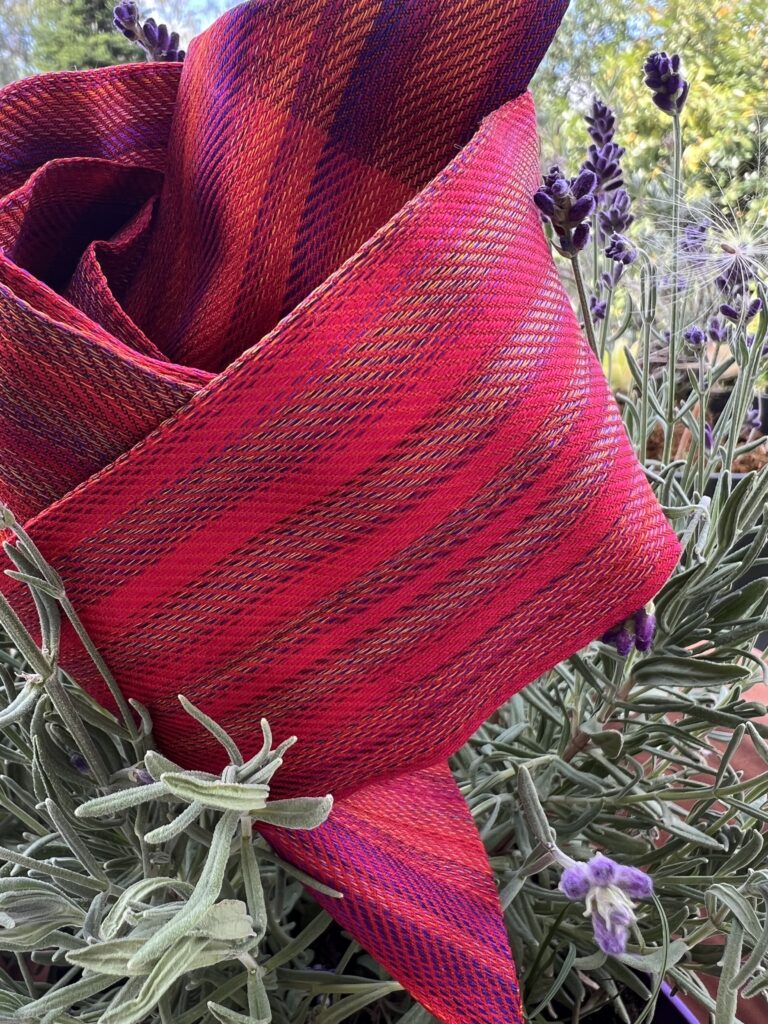 Twilly d'exception Tohora en soie de mûrier lourde 22 momme rouge rubis et violet posé sur un buisson de lavande